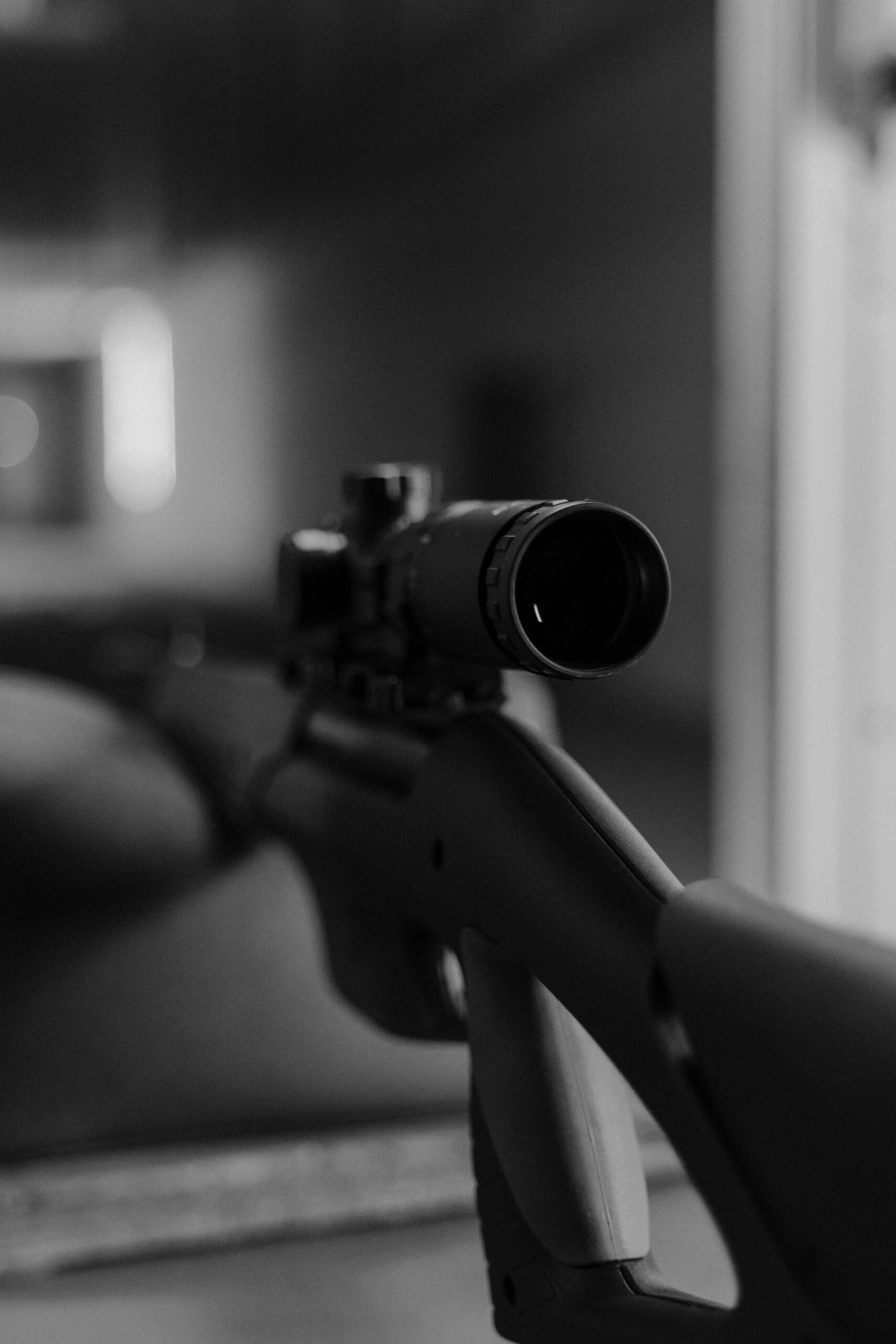 Monochrome image of a sniper rifle focusing on the scope in a soft-focus environment.