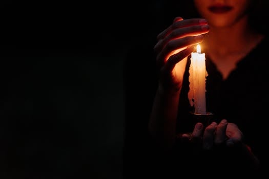 Close-up of a person in the dark holding a single lit candle, creating a moody atmosphere.