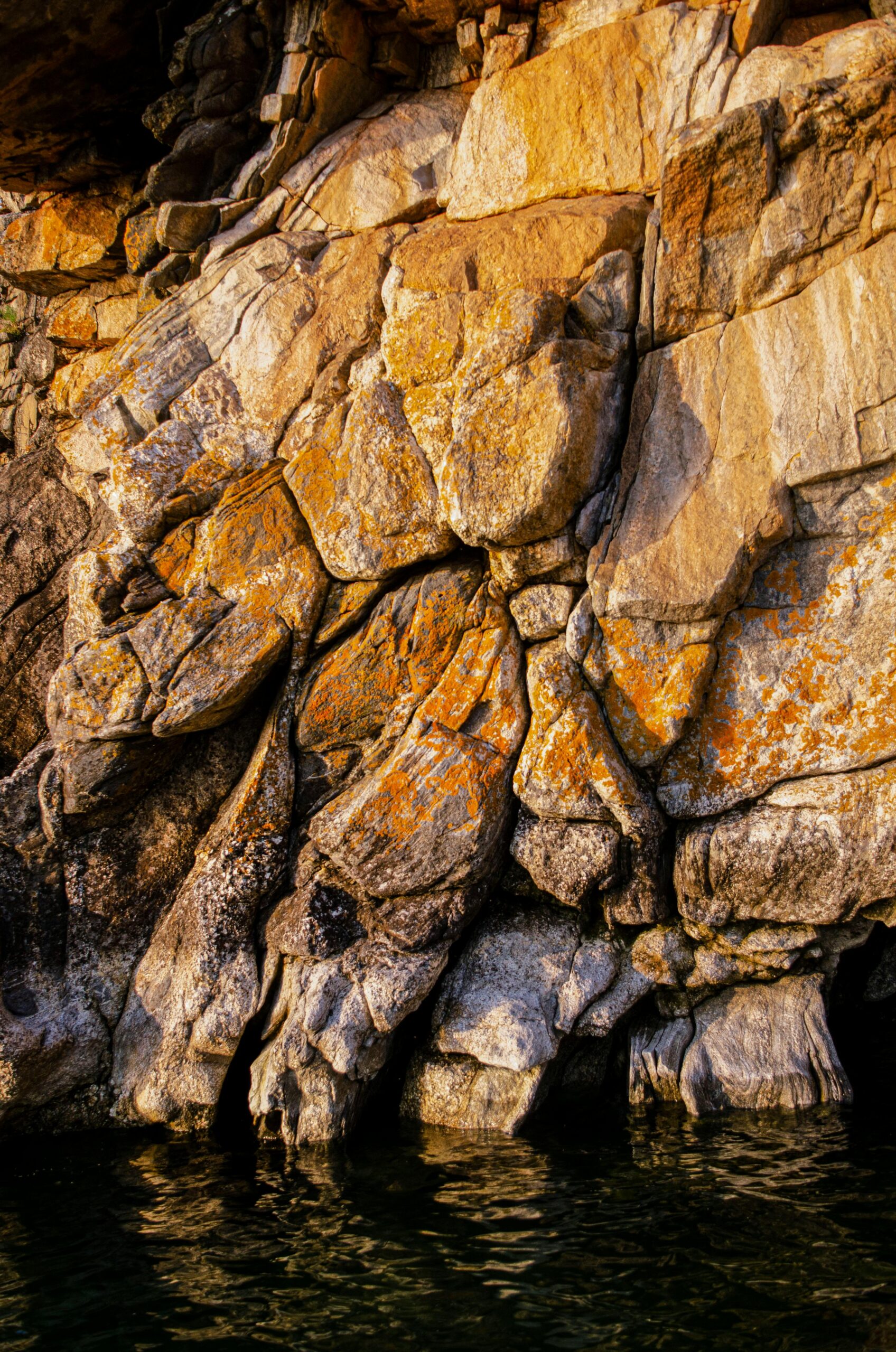 Sunlit rocky cliff with vibrant textures over calm water, perfect for nature backgrounds.