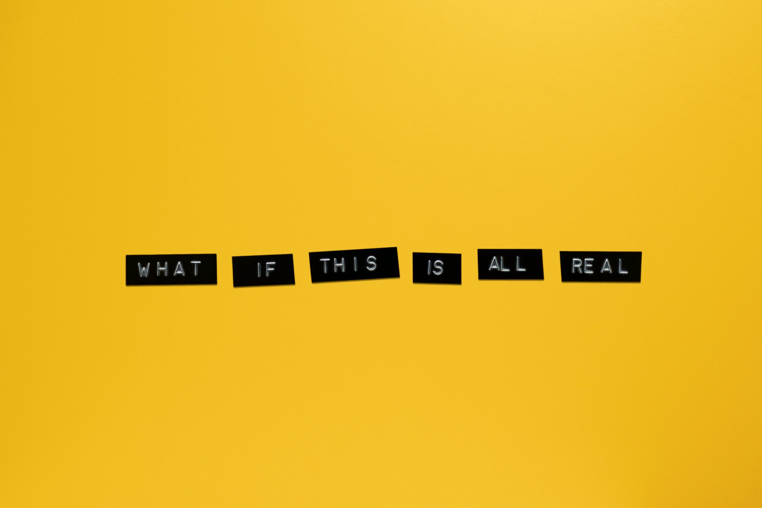 Minimalist text on vibrant yellow backdrop reading 'What if this is all real.'