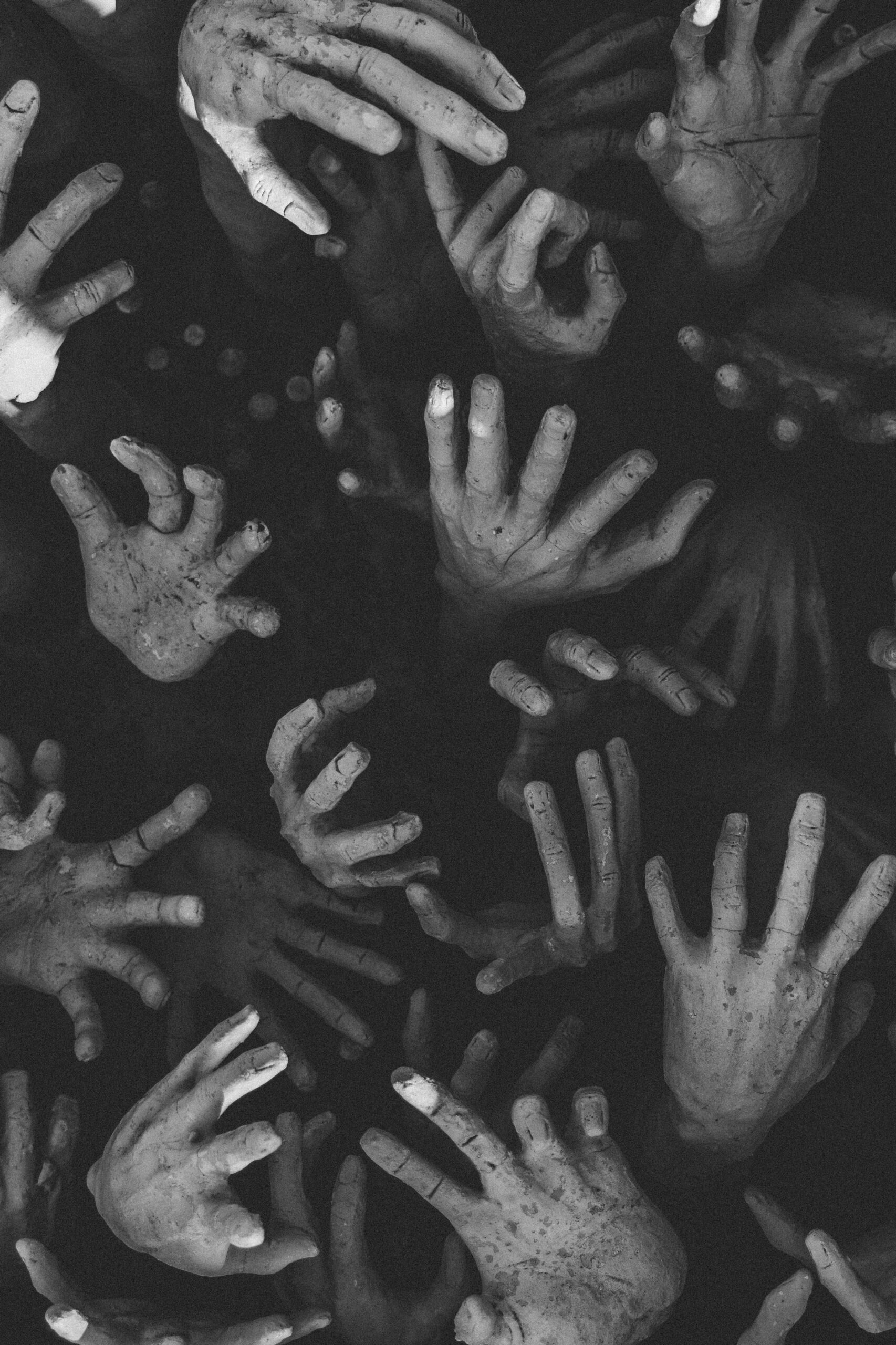 Dark monochrome sculpture of multiple hands reaching out, creating a haunting aesthetic.
