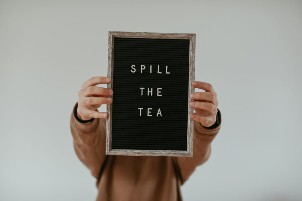 Person holding a letter board with the phrase 'Spill the Tea' against a white wall.