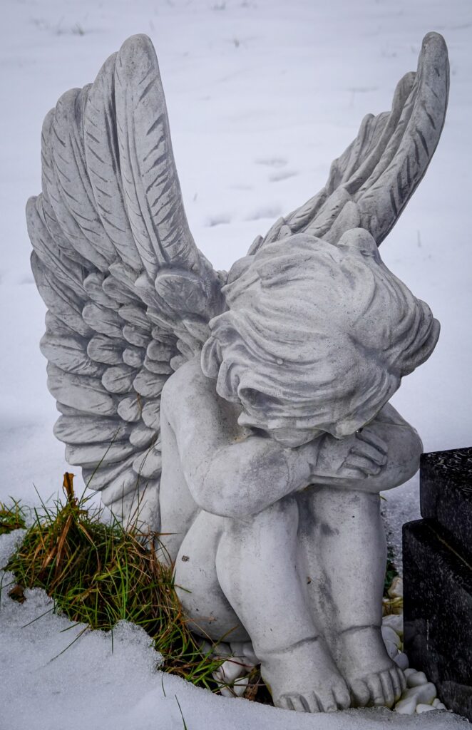 A peaceful angel figurine with wings seated in snow, evoking serenity and contemplation.