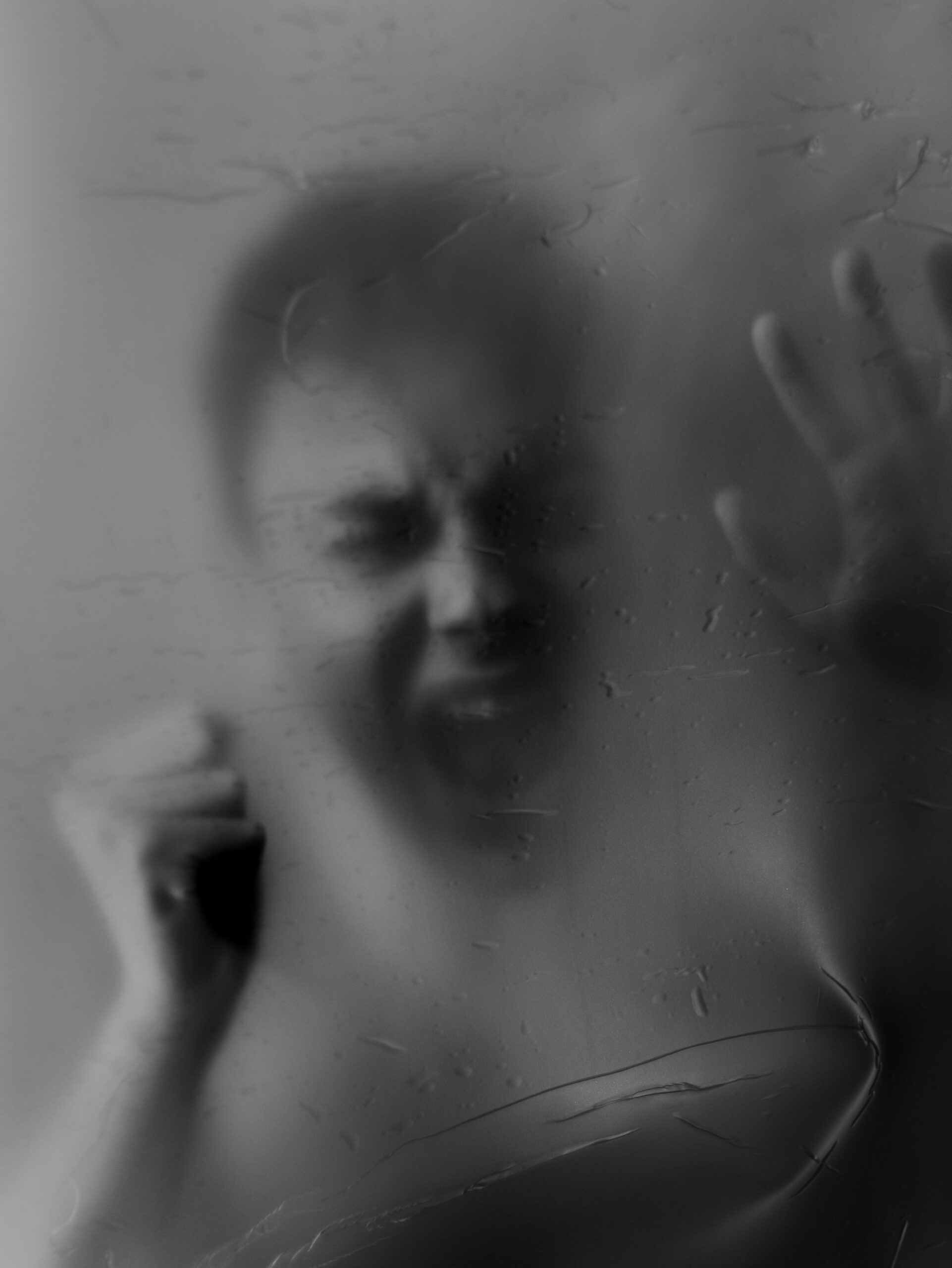 A haunting black and white image of a person in distress, pressing against a foggy surface.