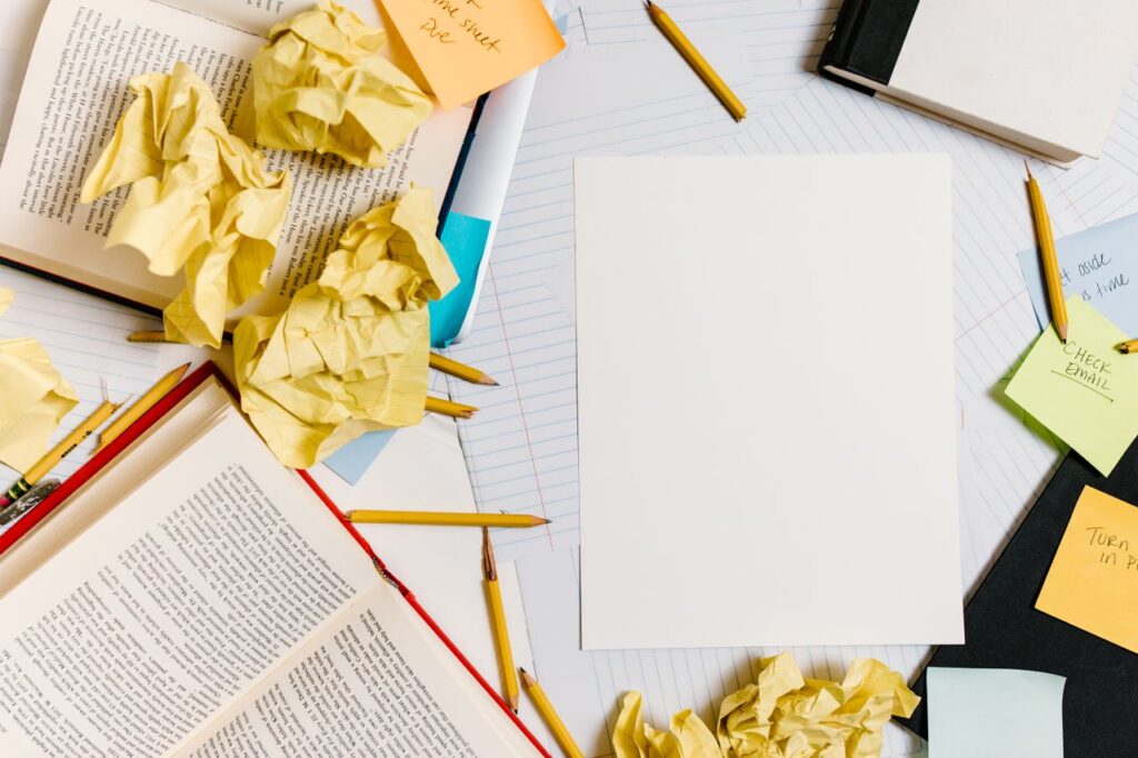 Overhead shot of a messy workspace with open books and crumpled papers.