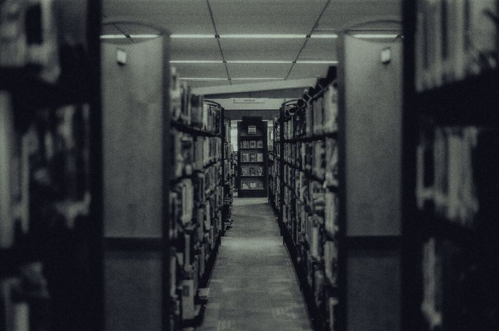 Atmospheric black and white photo capturing a library aisle with rows of shelves filled with books and a vanishing perspective.